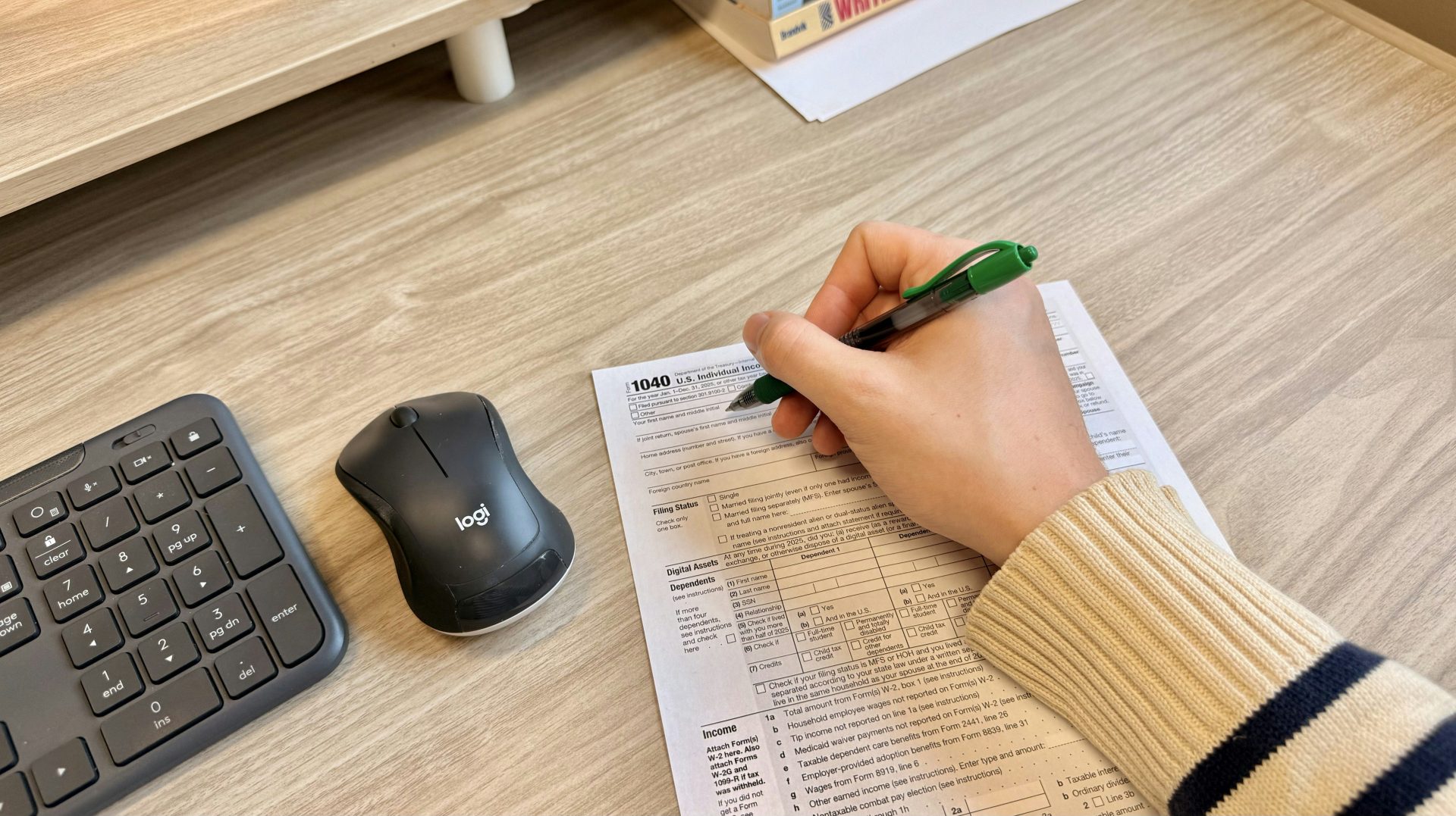 Hand writing on document next to keyboard and mouse.